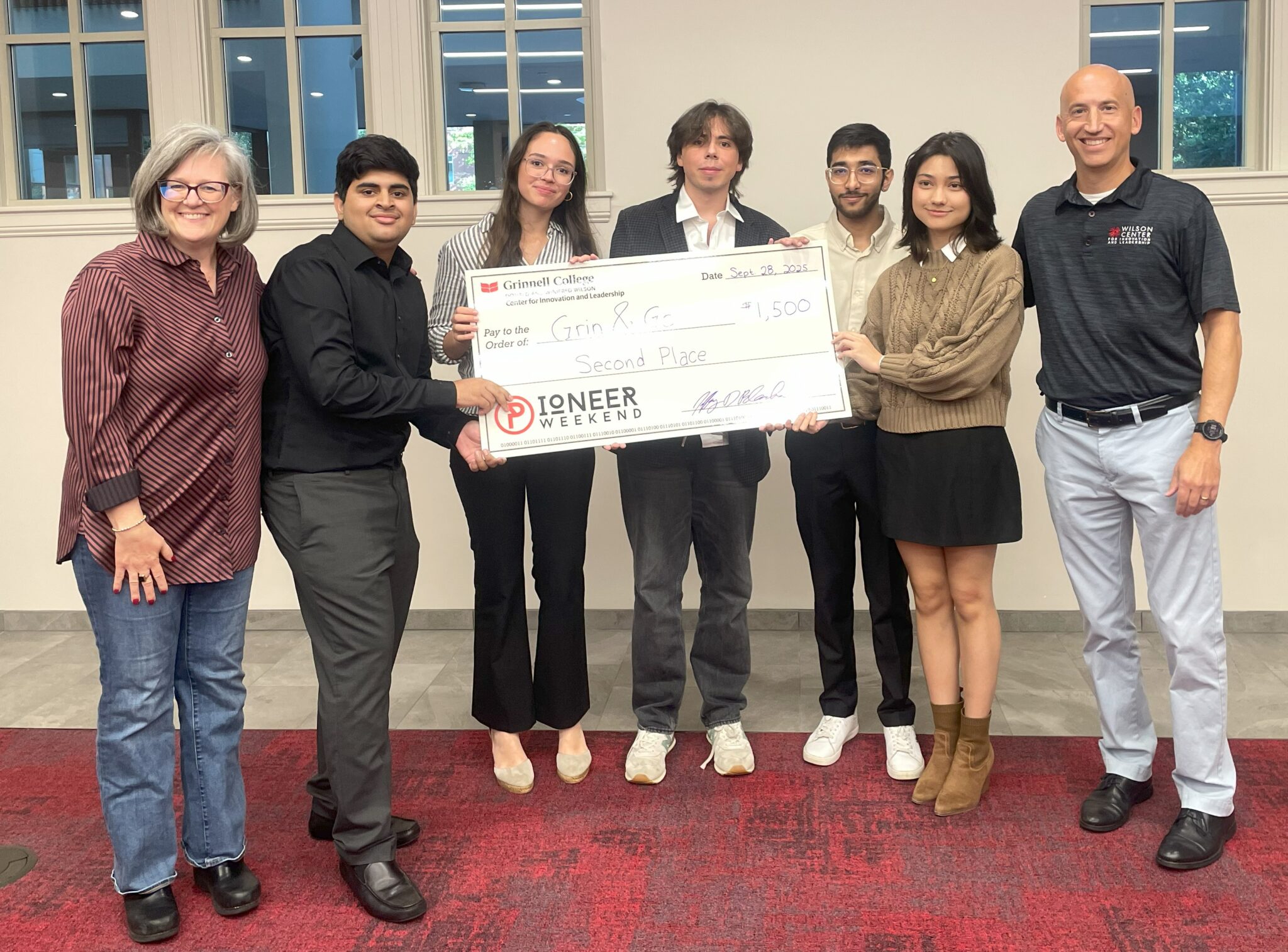 The Grin & Go team holding an oversized second-place check for $1,500 at Grinnell College's Pioneer Weekend, September 2025.